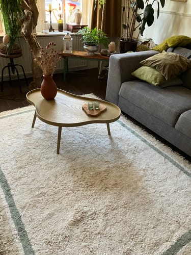 Beoordelaar toont de WOOOD Mae bijzettafel in alpaca-kleur in een sfeervolle woonkamer.