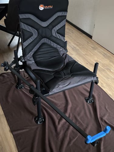 Recensent toont het POLE SUPPORT SYSTEM gemonteerd op een zwarte feederstoel binnenshuis.