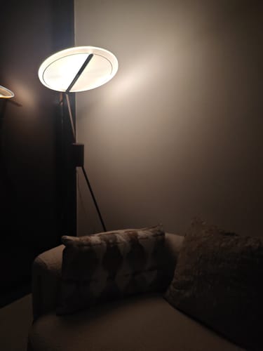 Reviewer's Spectra Arc Floor Lamp lit up in a cozy room, casting warm light beside a sofa.