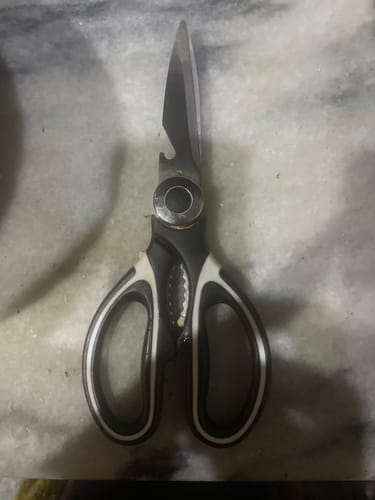 A reviewer's pair of multi-function kitchen scissors with black and white handles on a marbled surface.