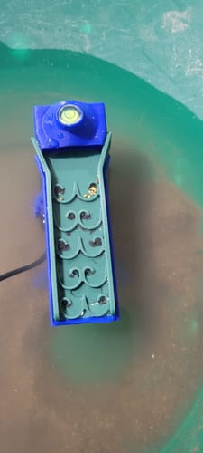 A reviewer's Dream Mat Pocket Sluice being used in a pan, with small gold flakes trapped in its green mat.