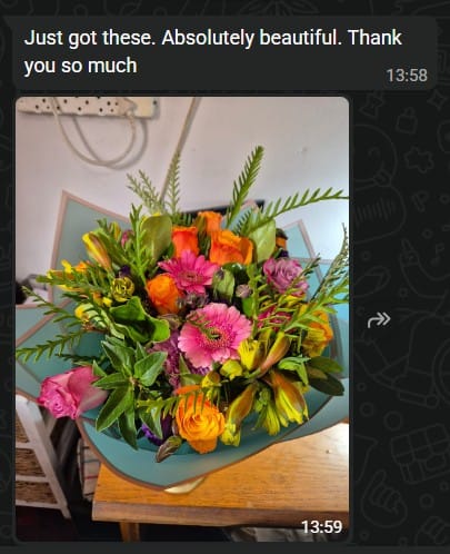 Customer's beautiful Lush and Lovely Bouquet with vibrant pink and orange roses and gerberas on a table.