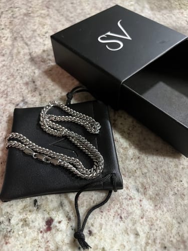 Un cliente muestra la Cadena Miami Cuban de 5mm sobre una bolsa negra, junto a la caja abierta del producto.