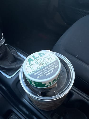 Customer's can of Mountain Wintergreen Nicotine Pouches resting on a travel mug in a car's cup holder.