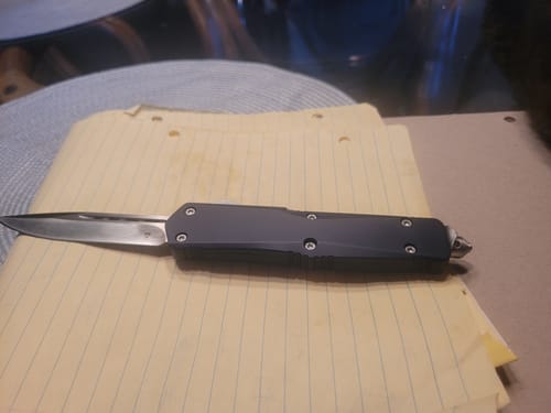 Customer's Blue Ghost OTF Knife with its dark handle and extended blade resting on yellow paper.