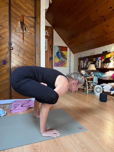 Reviewer in a black V Back Jumpsuit holding a crow yoga pose, showing the garment's flexible fit.