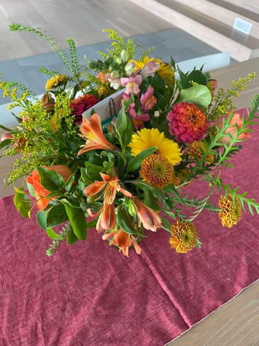 Customer's top-down view of the vibrant Happiness in a Jar flower arrangement on a red table runner.