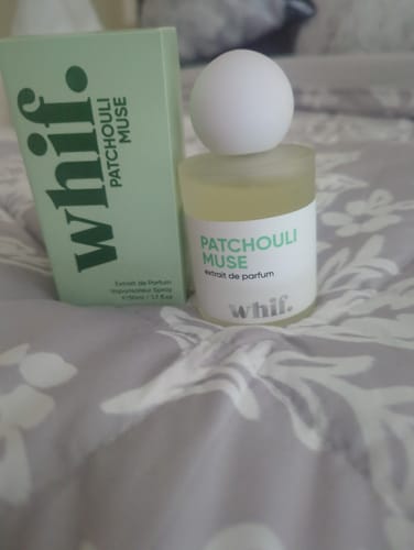 Reviewer's Patchouli Muse perfume bottle and its light green box resting on a patterned surface.
