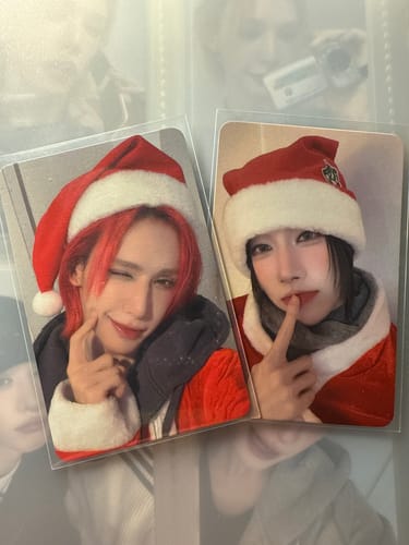 Customer displays two XLOV photocards from the fansign event, each featuring a person in a festive Santa hat inside a protective sleeve.