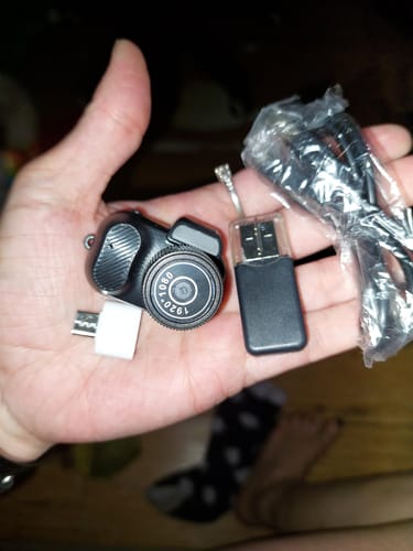 Reviewer holding the compact Retro Mini Keychain Camera and its accessories in their palm.