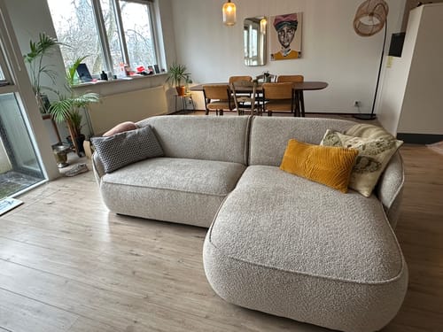 Recensent toont de greige bouclé Chubby hoekbank in een stijlvolle, lichte woonkamer.