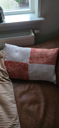 Recensent's Groove sierkussen in terra en grijs, liggend op een bruine bank.