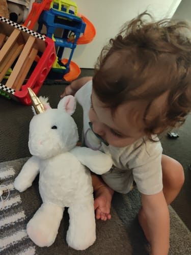 Reviewer's child sits closely with the soft, white Bubbly the Unicorn plush toy.