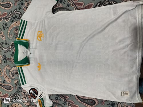 Recensore mostra la toppa realistica della Europa League sulla sua maglia bianca e verde.