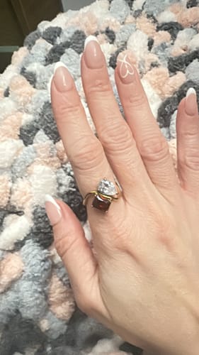 Customer's hand wearing the Navae Birthstone Ring, showing the two distinct red and clear stones on the shiny gold band.