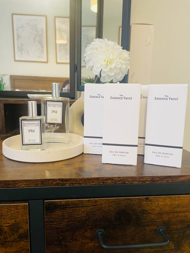 Customer's two bottles of 782 perfume and their boxes displayed on a dark wooden dresser in a bedroom setting.