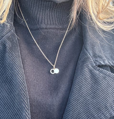 Customer wearing the gold Empty Tomb Pendant Necklace over a black turtleneck and jacket.