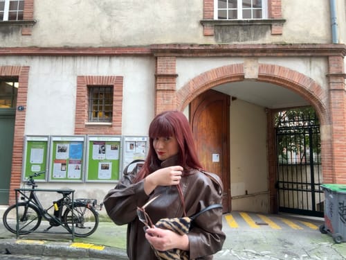 Reviewer on a street wearing the brown Tie Asymmetric Faux Leather Bomber Jacket.