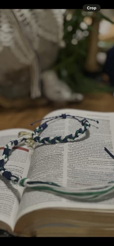 Reviewer's woven DAVID Bracelet in blue, green, and white resting on the pages of an open book.