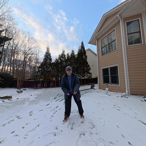 Reviewer smiling while wearing their warm Parka "Slate" in a snowy backyard.