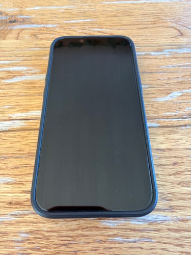 Foto eines Rezensenten, das ein iPhone mit aufgebrachter 3-in-1-Schutzfolie auf einem Holztisch zeigt.