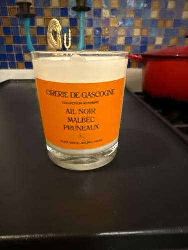 Reviewer's Black Garlic, Malbec, Prune Blend Candle in a glass jar with an orange label, sitting on a kitchen counter.
