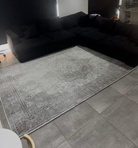 A customer's light grey patterned Relax Mat on the tiled floor of a living room next to a sofa.