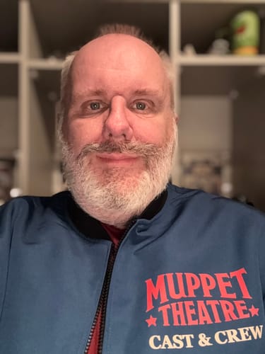Reviewer in the blue Muppets bomber jacket, showing the 'Muppet Theatre Cast & Crew' design.
