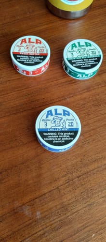 Customer's tin of Chilled Mint Nicotine Pouches on a wooden table, alongside two other flavors from the same brand.