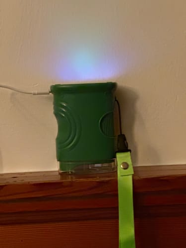 Rezensent zeigt das grüne Abenteuer-Mikroskop auf einer Holzoberfläche, während es mit eingeschaltetem Licht aufgeladen wird.