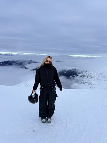 Reviewer on a snowy mountaintop wearing the baggy black wear-resistant snow pants.