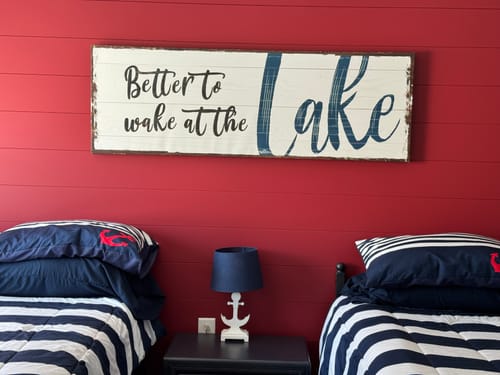 Customer's Better To Wake At The Lake Sign hanging on a red wall above two beds.
