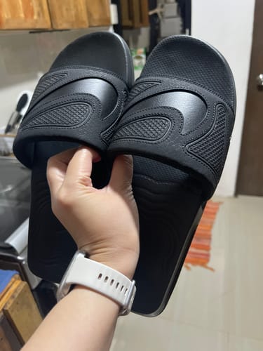 Customer's hand holding up a pair of new, all-black Nike Men's Air Max Cirro Slides.