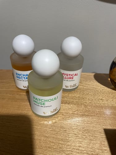 Customer's Patchouli Muse perfume bottle in frosted glass, shown with two other fragrances on a wooden surface.