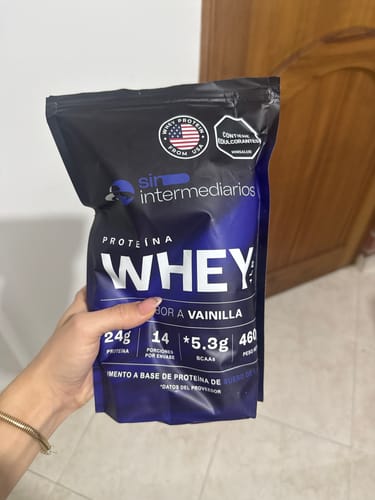 Cliente sostiene la bolsa negra y morada de Proteína Whey sabor vainilla.