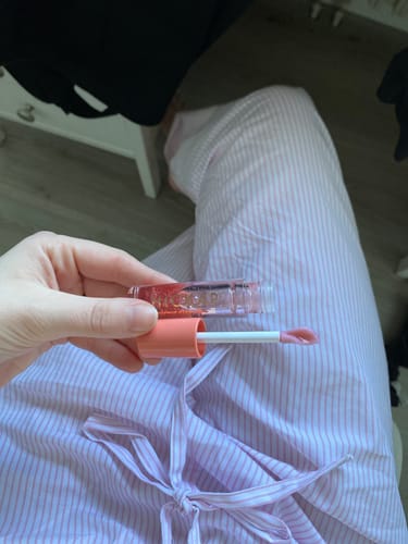 Kund som håller i en öppen Mirror Glaze Lip Oil och visar applikatorn med glansig produkt.