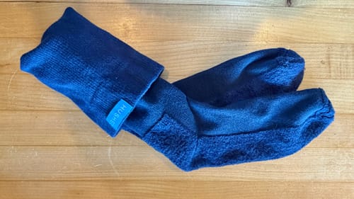 Customer's blue compression socks on a wood surface, with one sock folded down to show the discreet brand label at the top.