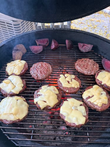 Cliente asando hamburguesas con queso y betabel en una parrilla de carbón.