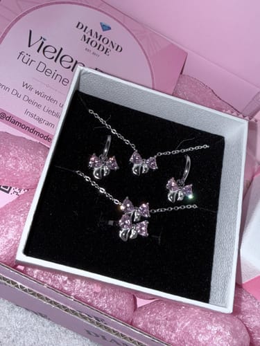 Ein Kunde zeigt das silberfarbene Sweet Bow Set mit rosa Zirkonia-Steinen in der offenen Schmuckschatulle.