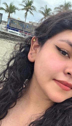 Clienta luciendo su Piercing Posie dorado con forma de flor en el cartílago de la oreja.