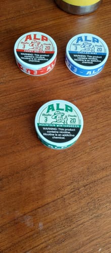 Customer's tin of Mountain Wintergreen Nicotine Pouches on a wooden table, alongside two other flavors.