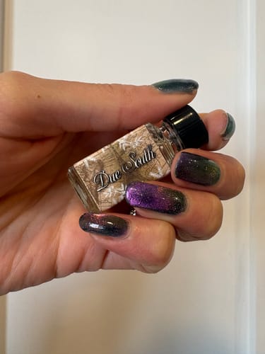 A customer's hand with dark, sparkling nail polish holding a small bottle of Due South perfume.