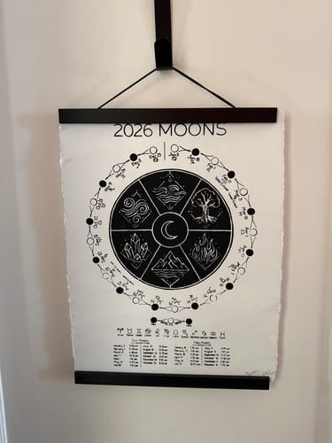 Reviewer's 2026 Moon Phase Calendar hanging on a wall in a black wooden holder.