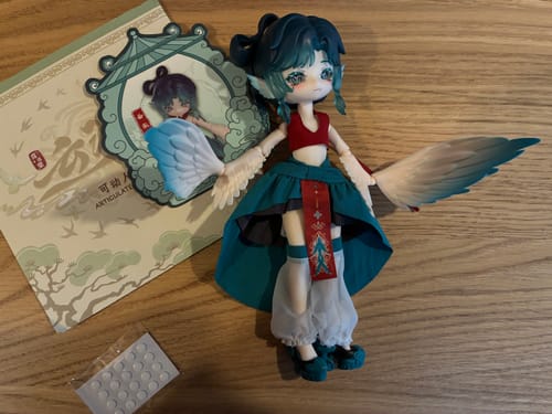 Reviewer's Luluya Cloud Feather Pavilion doll standing on its own, showing off its wings and teal outfit next to its card.