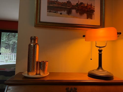 Customer's hand-hammered copper water bottle and matching cup on a wooden desk under a warm lamp.