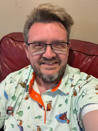 Close-up of a customer smiling while seated and wearing The Flintstones "Loyal Order of Dinosaurs' Tourney" polo.