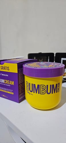 Cliente exibe o pote amarelo de Bumbum Cream (500g) ao lado da sua caixa roxa.