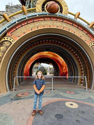Reviewer's child wearing the "Fiery Faces" short sleeve shirt at a dragon-themed park entrance.