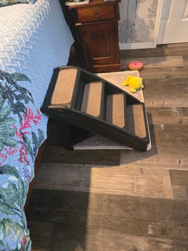 Customer's black Indoor Dog Steps placed on a mat beside a bed, as mentioned in the review.