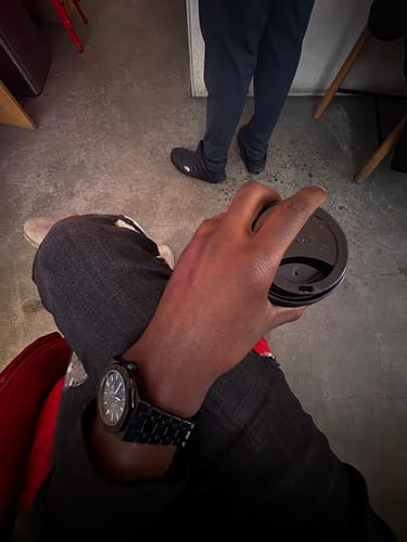 Reviewer wearing a black Lucky Fours® Oceanus watch while sitting and holding a coffee cup.